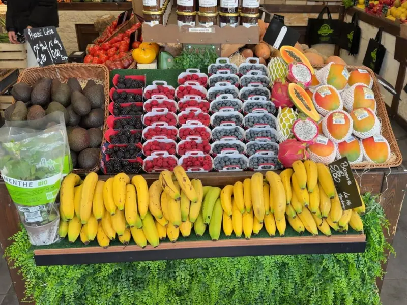 Étal de bananes, framboises, mûres, myrtilles, mangues, papayes et fruits du dragon, à côté d'un panier d'avocats