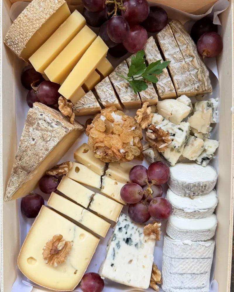 Plateau de fromages dans une caisse en bois : pâtes dures, tomme, bleu et bûche de chèvre, avec raisin rouge et cerneaux de noix
